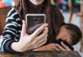 Mother wearing hijab using mobile phone while breastfeeding baby.
