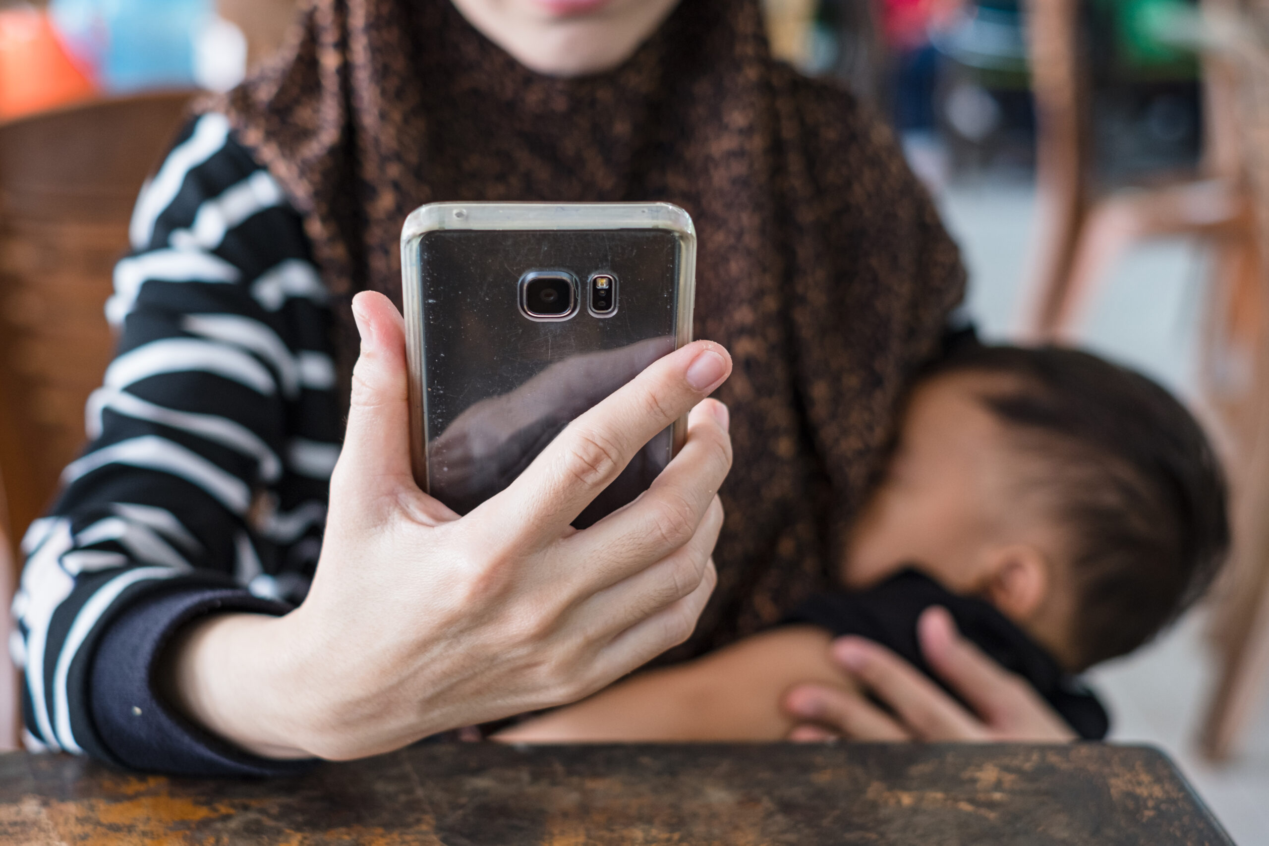 Mother wearing hijab using mobile phone while breastfeeding baby.